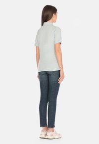 Polo shirt azzurro chiaro con maniche corte, abbinato a jeans slim-fit scuri e sneakers rosa chiaro. Design semplice, texture liscia.