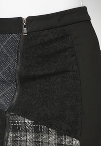 Falda negra con paneles texturizados con patrones florales, diseño a cuadros y cierre de cremallera en el lateral. El material combina telas tejidas y lisas.