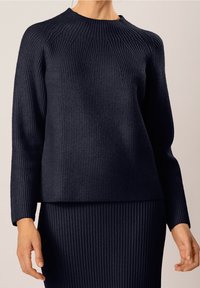 Granatowy sweter z prążkowanego dzianiny z wysokim kołnierzem i długimi rękawami, z teksturowanymi pionowymi paskami tworzącymi strukturalny wygląd.