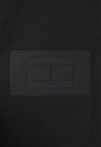 Černá látková nášivka s texturovaným povrchem, obsahující tři horizontální obdélníkové výřezy. Hladké okraje a prošívané okraje pro zvýšení odolnosti.