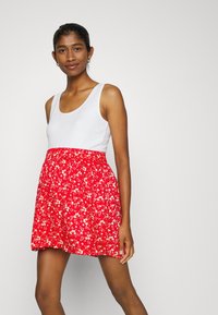 Vestido floral vermelho com um corpete justo branco e cintura elástica. Apresenta pequenas flores brancas sobre um fundo vermelho vibrante. Design curto e casual.