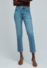 Jeans de cintura alta en un tono azul claro, con pernera ajustada y dobladillo sin rematar. Hechos de denim con un ligero desgaste y diseño de cinco bolsillos. Costuras visibles.