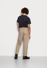Calças bege com corte reto e bolsos laterais, combinadas com uma t-shirt preta ajustada. Botas pretas de tornozelo completam o look.