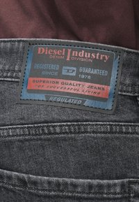 Primer plano de la etiqueta de Diesel Industry en unos jeans gris oscuro, con texto sobre calidad superior y registro desde 1978.