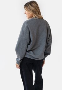 Szary, oversize'owy sweatshirt z prążkowanym dołem i mankietami, z opadającymi ramionami i szczotkowaną fakturą, noszony z czarnymi spodniami.