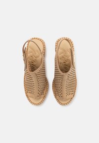 Sandales en suède perforé beige avec une sangle arrière, semelle plate et bords surpiqués. Dotées d'une semelle intérieure texturée avec l'inscription de la marque.