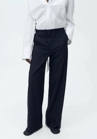 Kape wide-leg dalam navy gelap dengan garis vertikal, dilengkapi dengan pinggang elastik dan tali serut serta tekstur kain yang halus.