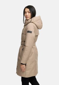 Beige polstret frakke med hætte, bælte i taljen, sidelommer og mærke på ærmet. Glat tekstur og knælangt design.