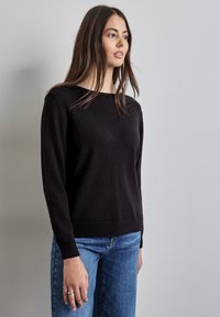 Maglione nero con scollatura rotonda, maniche lunghe e orlo a coste. Abbinato a jeans blu, con texture liscia e design aderente.