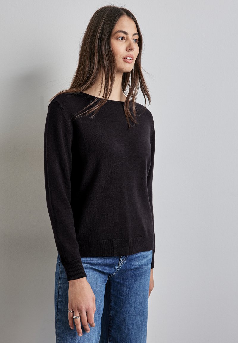 Maglione nero con scollatura rotonda, maniche lunghe e orlo a coste. Abbinato a jeans blu, con texture liscia e design aderente.