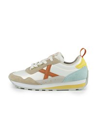 Sneaker featuring white leather, beige suede, and blue accents. Tan cross logo, yellow heel tab, and a textured outsole in contrasting colors.