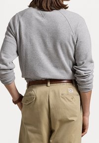 Sudadera gris con cuello redondo y mangas raglán, combinada con pantalones kaki que tienen bolsillos traseros y un cinturón de cuero marrón.