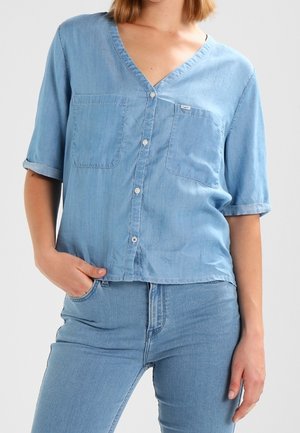 Himmelblaues Jeanshemd mit kurzen Ärmeln, V-Ausschnitt, zwei Brusttaschen und Knopfverschluss. Weicher Stoff, leicht lockere Passform.