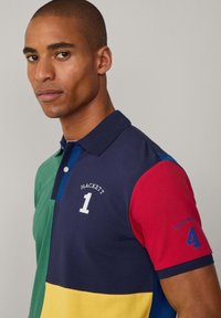 Poloshirt met een veelkleurig ontwerp met groene, blauwe, marineblauwe, rode en gele secties. Geborduurde '1' en '4', gemaakt van katoen.