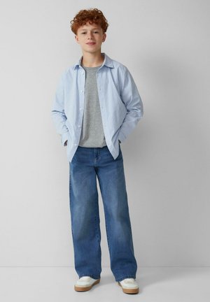 Hellblau gestreiftes Hemd über einem grauen T-Shirt, kombiniert mit locker sitzenden blauen Jeans und weißen Sneakers mit beigen Akzenten.