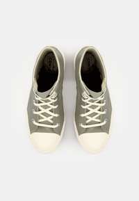 Zapatillas altas de lona verdes con punteras de goma blanca, ojales de metal y cordones color crema. Parte superior texturizada y suela lisa.