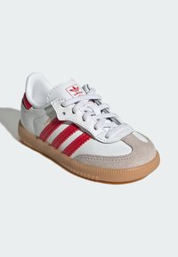 White and gray athletic shoe with red accents and three stripes, featuring a textured suede toe and a gum rubber sole.