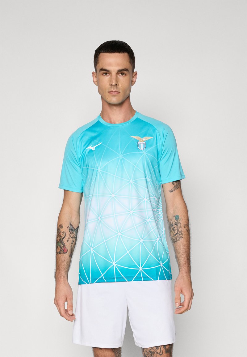 Světle modrý sportovní dres s krátkým rukávem, zdobený geometrickým vzorem, s logem na hrudi a kulatým výstřihem, doplněný bílými šortkami.