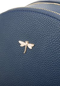 Blauer strukturierter Leder-Rucksack mit einem goldenen Libellenemblem auf der Vorderseite. Zwei Metallreißverschlüsse entlang der oberen Kante.