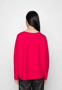 Pull rose vif à la coupe décontractée, encolure large et manches longues, associé à un pantalon en cuir noir. Texture lisse, design décontracté.