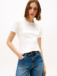 T-shirt de algodão branca com decote redondo, combinada com jeans azuis de cintura alta com um cinto preto. Detalhe de logotipo discreto na camisa.