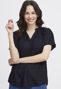 Haut noir à manches courtes avec une coupe décontract�ée, en tissu texturé, et un décolleté en V avec des accents froncés au niveau du col.