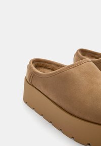 Barna, suede-szerű, slip-on cipők párnázott belső résszel, megemelt, vastag talppal és sima felülettel. Egyszerű dizájn, látható díszítések nélkül.