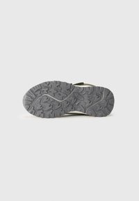 Suela de goma gris de una bota de senderismo con un patrón de relieve profundo y robusto para tracción en exteriores, mostrada sobre un fondo blanco liso.