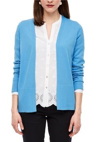 Svetle modrý kardigán, design s otevřeným předním dílem, žebrovaná textura, dvě přední kapsy, nošený přes bílou blůzku s vyšívanými detaily.