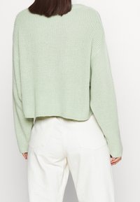 Lyhyt, pitkähihainen neule vaaleanvihreänä, jossa on teksturoitu kuvio. Yhdistetty korkeavyötäröisiin valkoisiin housuihin.