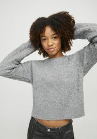 Maglione grigio corto con motivo a treccia, scollatura rotonda e polsini a costine, abbinato a pantaloni neri. Tessuto morbido e testurizzato.