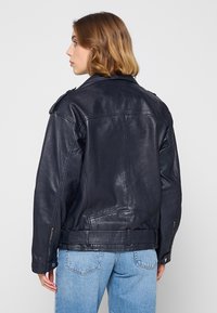 Marinblå läderjacka med strukturerad krage, axelsnibbar och sidofickor med dragkedja. Texturerad yta och en något avslappnad passform.