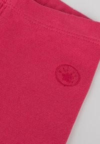 Tessuto di cotone rosa con una superficie liscia; presenta un logo circolare impresso vicino alla cucitura. La cucitura dei bordi è visibile.