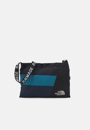 Czarna i turkusowa torba na ramię o prostokątnym kształcie, wykonana z wytrzymałej tkaniny; posiada kontrastowe logo, regulowany pasek i zapięcie na zatrzask.