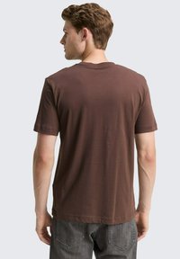 Bruine korte mouwen t-shirt gemaakt van zacht stof, met een ronde halslijn en een relaxte pasvorm, gecombineerd met grijze jeans.