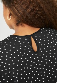 Top nero con pois bianchi, caratterizzato da un'apertura a chiave sul retro del collo, realizzato in un tessuto morbido e elastico.
