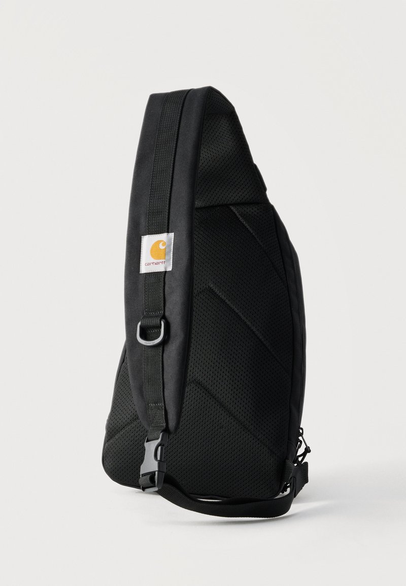 Mochila bandolera acolchada negra con parche del logo de Carhartt, correa ajustable y anilla en D de metal, mostrada sobre un fondo claro liso.