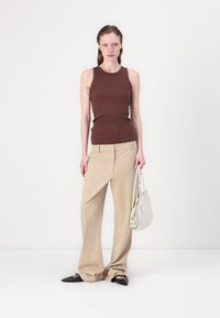 Brun uten ermer topp, beige bredbein bukser, svarte spisse sko, holder en hvit veske. Enkel design, glatt tekstur, minimal detaljer.