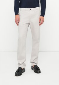 Pantaloni drepți din bumbac gri deschis, cu închidere cu buton și bucle pentru curea. Asortați cu loafers negri, cu detalii de franjuri.