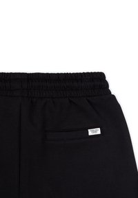 Pantalones deportivos negros con una cinturilla elástica, que cuentan con un pequeño bolsillo trasero con una etiqueta. La tela es suave y elástica.
