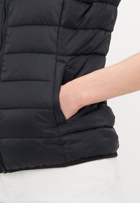 Svart vadderad väst med horisontell quiltad struktur och dragkedja, med en sidoficka synlig på vänster sida.