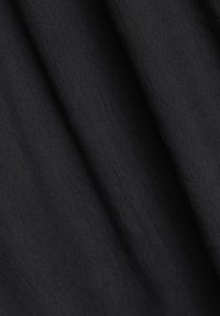 Sort stof med en struktureret overflade, der har fine nuancer og en blød glans. Draperingen skaber bløde folder.
