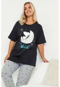 Camiseta de algodón negra con un gráfico de Snoopy en purpurina plateada tumbado sobre una luna, acompañado del texto "Nota para mí mismo: RELÁJATE". Combinada con pantalones grises con estampado.