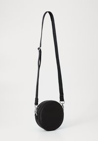 Borsa a tracolla rotonda nera con chiusura zip, tracolla regolabile e hardware in argento lucido. Texture liscia, design minimalista.