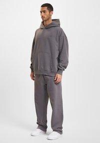 Gray hooded sweatshirt with front pocket, relaxed fit, and matching gray sweatpants. White sneakers complete the outfit.