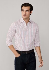 Chemise légère à boutons, blanche avec un motif à carreaux rouge et bleu, manches longues retroussées jusqu'aux coudes, assortie à un jean foncé et à une ceinture noire.