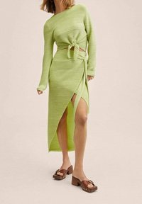 Jasnozielony, prążkowany komplecik składający się z krótkiego swetra związanego w talii oraz spódnicy z wysokim rozcięciem. Brązowe sandały na słupku z ozdobnymi elementami.