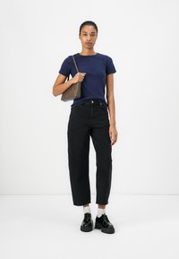T-shirt en coton marine associé à un jean noir taille haute. Présente une coupe ajustée, des manches courtes et des chaussures noires imposantes. Accessoire : petit sac marron.