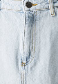 Světlé modré džíny z denimu s viditelnými záhyby, žlutým prošíváním, černým kovovým knoflíkem a standardním designem s pěti kapsami.