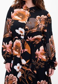 Abito nero con motivo floreale, caratterizzato da grandi fiori arancioni, rosa e bianchi. Maniche lunghe, chiusura frontale con bottoni e vita regolabile con cordoncino per una vestibilità personalizzabile.